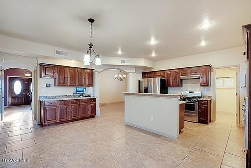 kitchen with arched walkways, a kitchen island, appliances with stainless steel finishes, hanging light fixtures, and light countertops