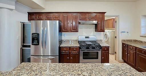 kitchen with stainless steel appliances, washer / dryer, under cabinet range hood, and light stone counters