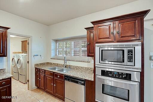 kitchen with light tile patterned floors, light stone counters, stainless steel appliances, separate washer and dryer, and a sink