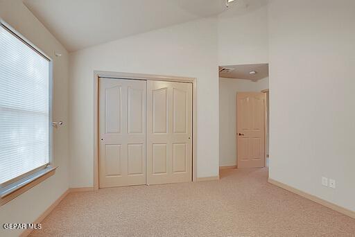 unfurnished bedroom with lofted ceiling, a closet, light colored carpet, and baseboards