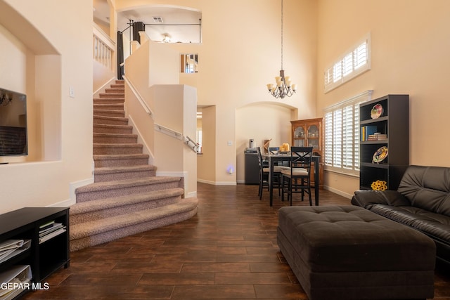 living room with a towering ceiling, stairway, an inviting chandelier, dark wood-type flooring, and baseboards