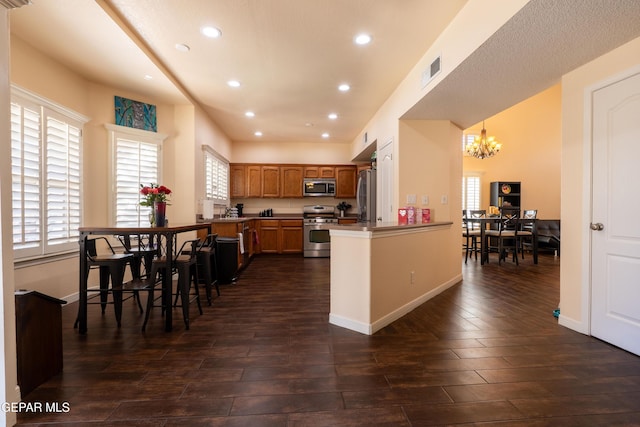 kitchen featuring visible vents, dark wood finished floors, a peninsula, stainless steel appliances, and a notable chandelier