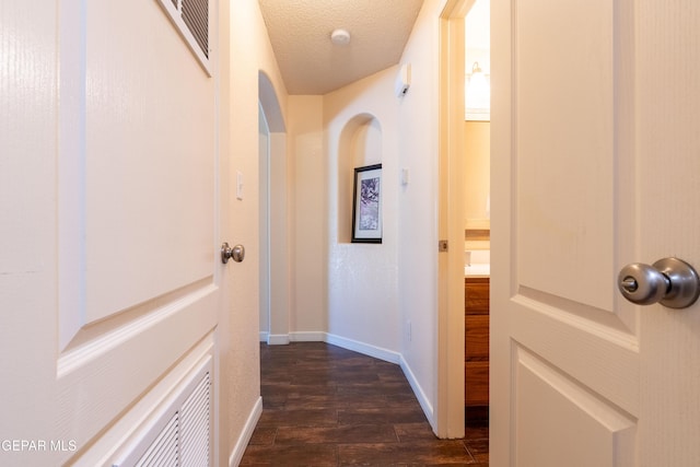 corridor featuring dark wood finished floors, a textured ceiling, and baseboards