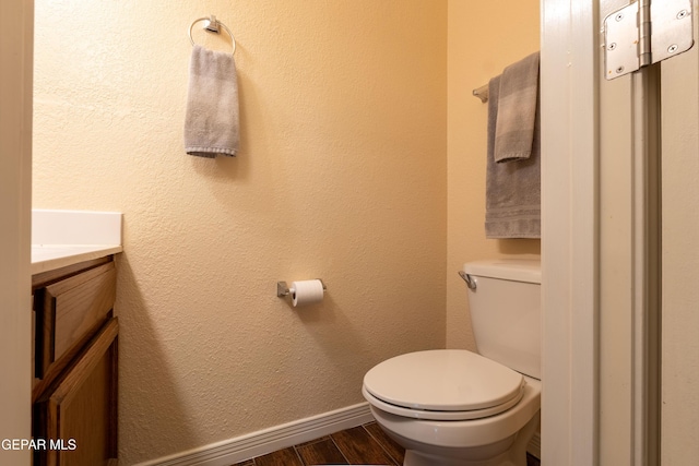 bathroom featuring baseboards, a textured wall, toilet, wood finished floors, and vanity