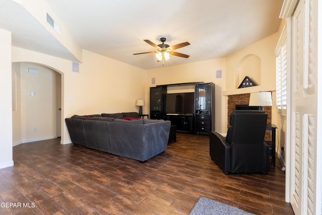 living area featuring arched walkways, ceiling fan, dark wood-style flooring, visible vents, and baseboards