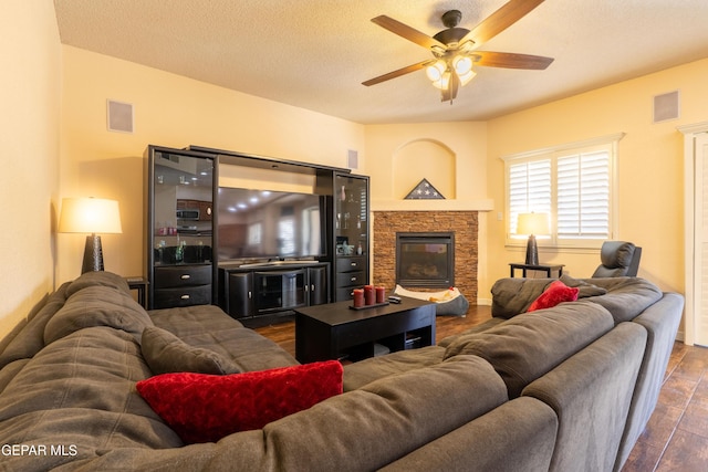 living room with dark wood-style floors, visible vents, a stone fireplace, and a ceiling fan