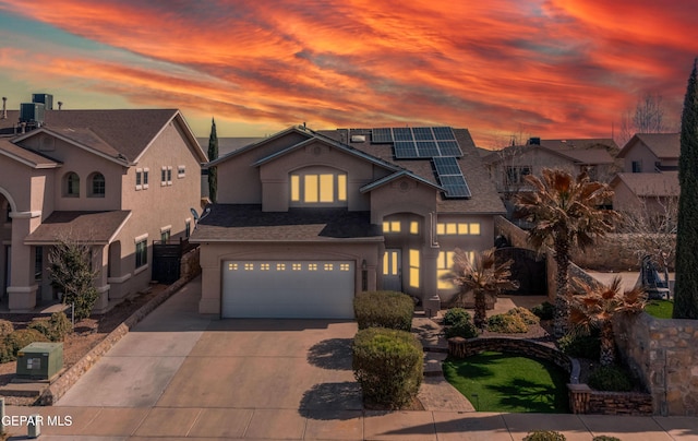 view of front of home with a garage, a shingled roof, concrete driveway, cooling unit, and roof mounted solar panels