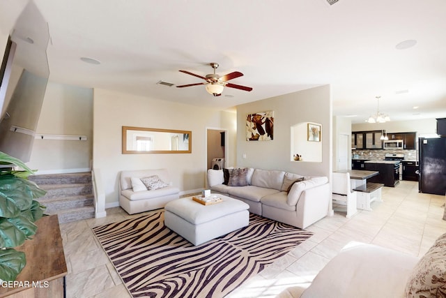 living area with ceiling fan with notable chandelier, stairway, visible vents, and baseboards