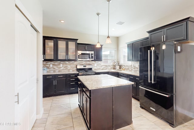 kitchen with visible vents, hanging light fixtures, appliances with stainless steel finishes, a center island, and glass insert cabinets