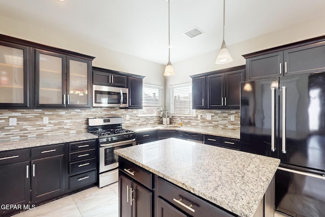 kitchen with a center island, decorative light fixtures, stainless steel appliances, visible vents, and glass insert cabinets