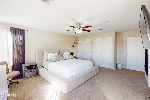 bedroom featuring light colored carpet, visible vents, ceiling fan, and two closets