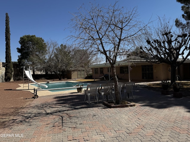 view of swimming pool featuring a patio, a water slide, a diving board, a fenced in pool, and a storage unit