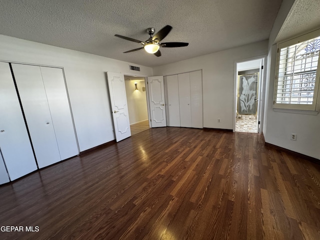 unfurnished bedroom with baseboards, visible vents, dark wood-style floors, a textured ceiling, and multiple closets