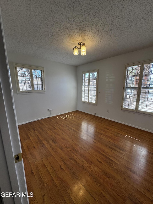 empty room featuring dark wood-type flooring, a textured ceiling, and baseboards