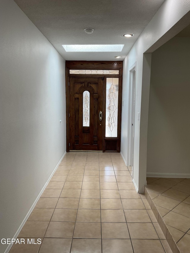 foyer with light tile patterned floors, a skylight, and baseboards