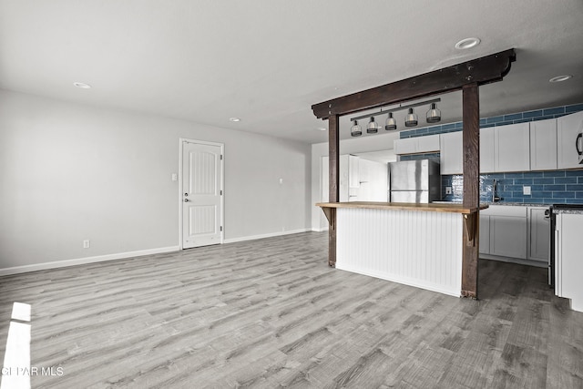 kitchen with tasteful backsplash, light wood-style flooring, freestanding refrigerator, open floor plan, and baseboards