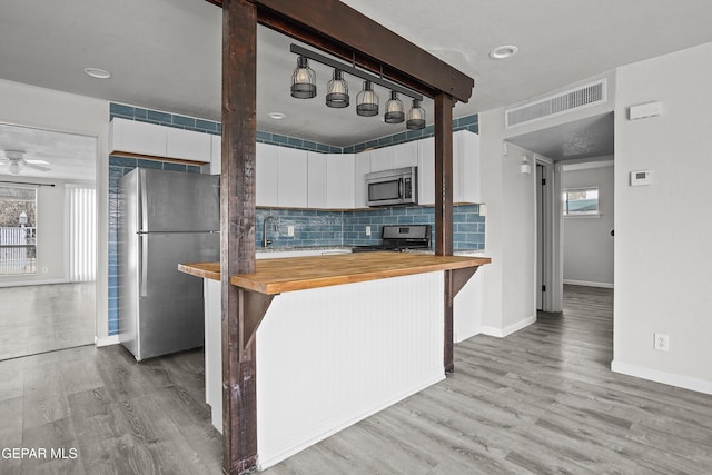 kitchen featuring visible vents, white cabinets, decorative backsplash, butcher block counters, and appliances with stainless steel finishes