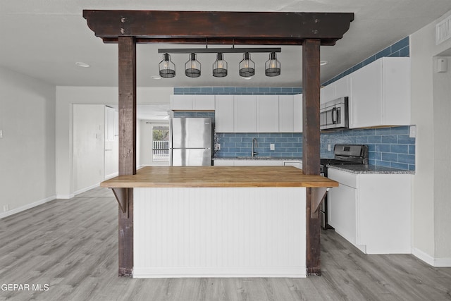 kitchen with butcher block counters, a sink, appliances with stainless steel finishes, light wood-type flooring, and decorative backsplash