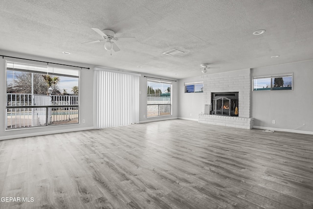 unfurnished living room featuring a ceiling fan, a brick fireplace, a textured ceiling, wood finished floors, and baseboards