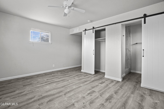 unfurnished bedroom with a barn door, baseboards, visible vents, wood finished floors, and a closet