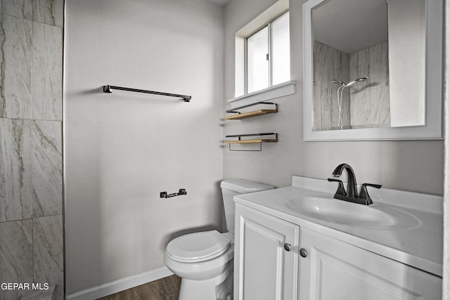 bathroom with baseboards, a shower, toilet, wood finished floors, and vanity