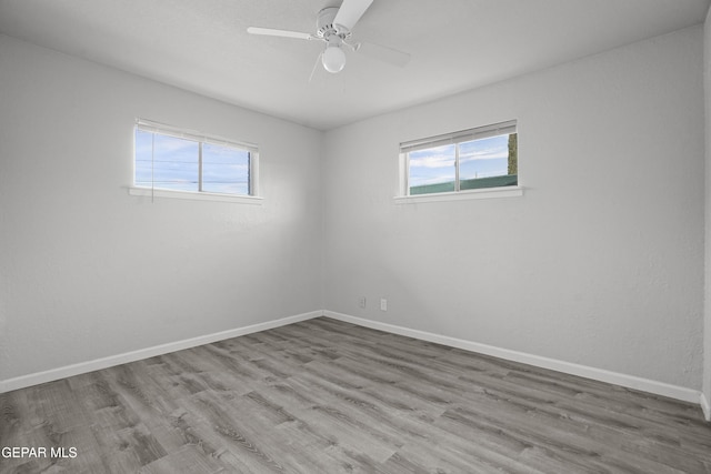 spare room featuring a healthy amount of sunlight, ceiling fan, baseboards, and wood finished floors