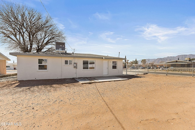 rear view of house featuring central AC, fence, a mountain view, and stucco siding