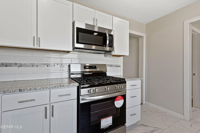 kitchen with light stone counters, white cabinetry, marble finish floor, appliances with stainless steel finishes, and tasteful backsplash