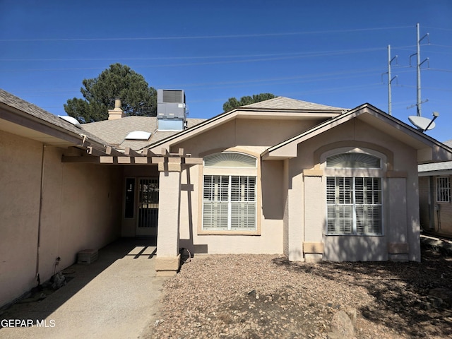 exterior space featuring a shingled roof, central AC unit, and stucco siding