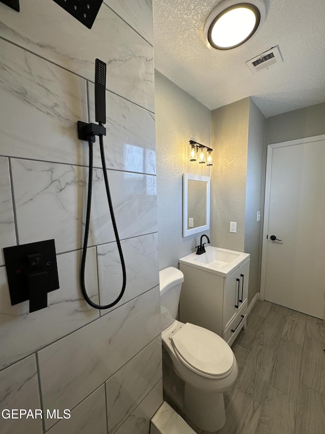 bathroom with a textured ceiling, toilet, vanity, visible vents, and a shower