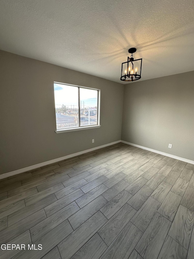 unfurnished room featuring light wood-style flooring, a textured ceiling, a chandelier, and baseboards