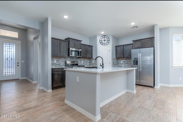 kitchen with a kitchen island with sink, dark brown cabinetry, visible vents, light countertops, and appliances with stainless steel finishes