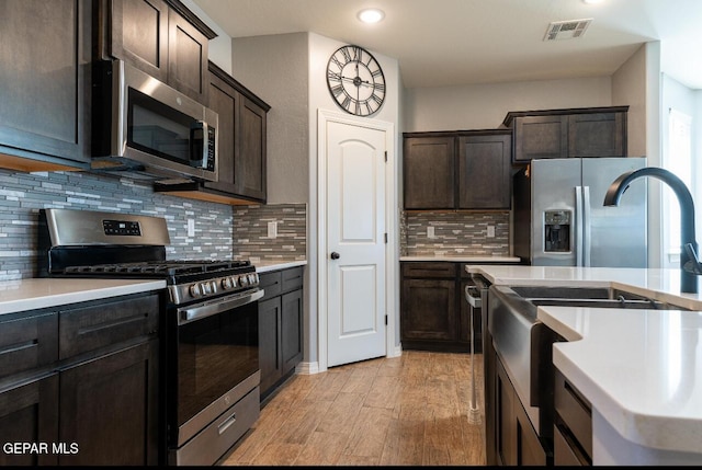 kitchen featuring stainless steel appliances, dark brown cabinets, light countertops, and visible vents