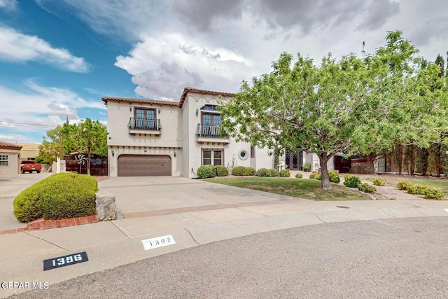 mediterranean / spanish house featuring driveway, a balcony, a tiled roof, an attached garage, and stucco siding