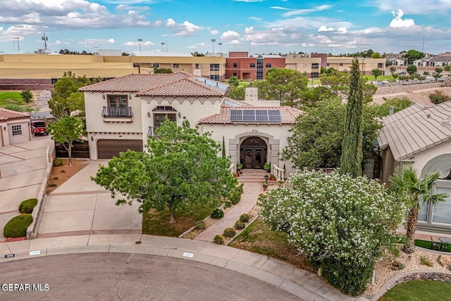 mediterranean / spanish house with concrete driveway, a tiled roof, an attached garage, roof mounted solar panels, and stucco siding