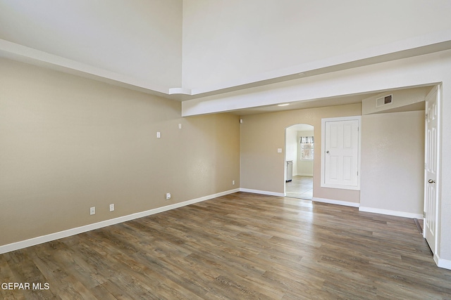 spare room with dark wood-style floors, arched walkways, visible vents, and baseboards