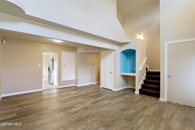 empty room featuring baseboards, arched walkways, wood finished floors, a high ceiling, and stairs