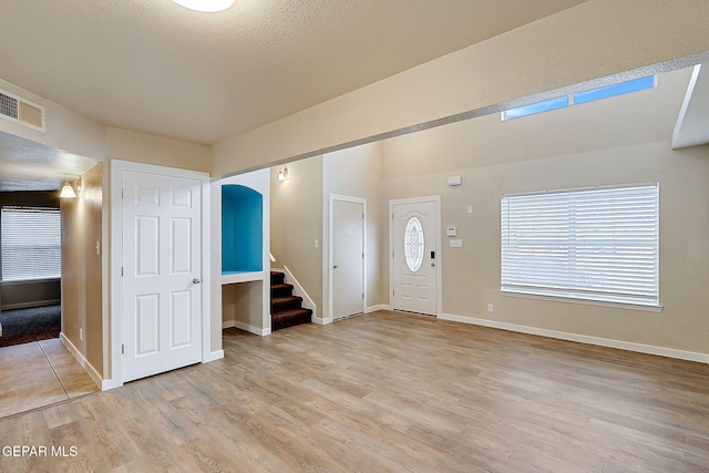 entrance foyer featuring baseboards, visible vents, stairs, a textured ceiling, and light wood-style floors