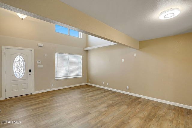 entryway featuring beam ceiling, light wood-style flooring, baseboards, and a textured ceiling