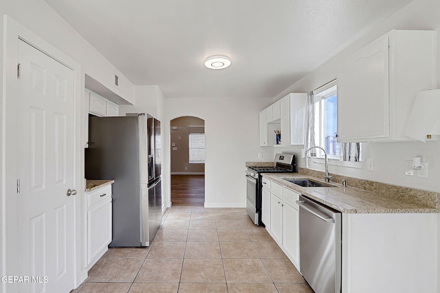 kitchen featuring light tile patterned floors, appliances with stainless steel finishes, a sink, and white cabinetry