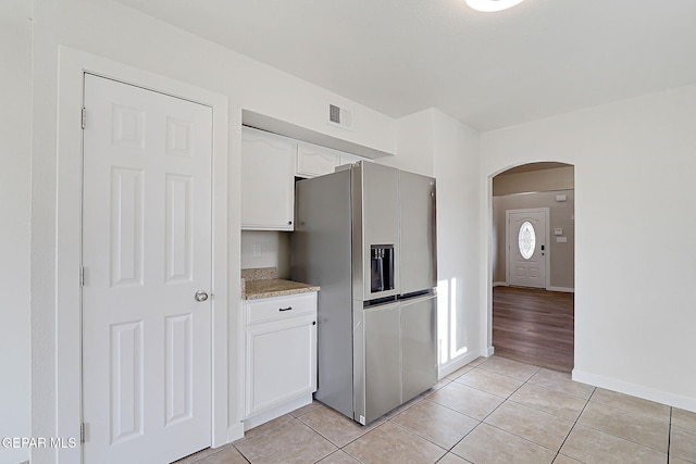 kitchen featuring arched walkways, light tile patterned floors, visible vents, white cabinets, and stainless steel fridge with ice dispenser