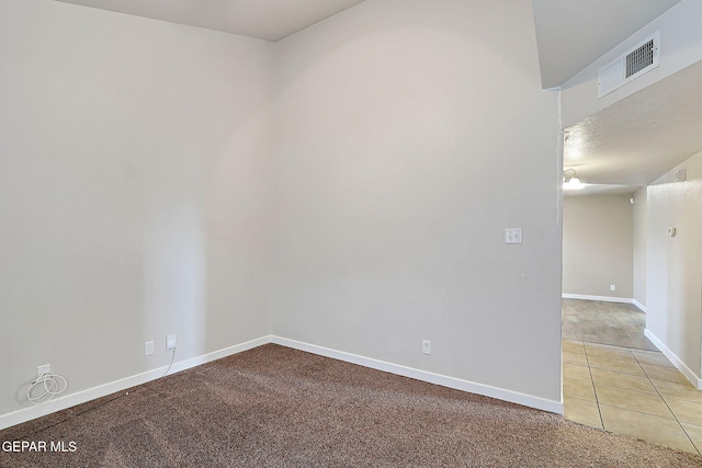 spare room featuring visible vents, baseboards, tile patterned floors, carpet, and a textured ceiling