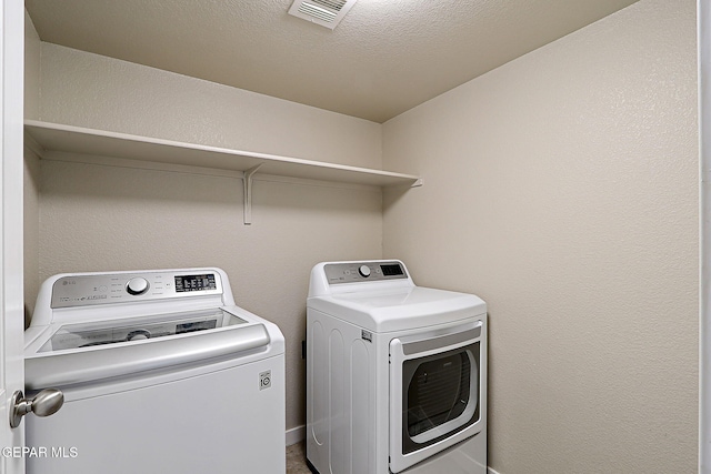 clothes washing area featuring laundry area, visible vents, washer and clothes dryer, a textured wall, and a textured ceiling