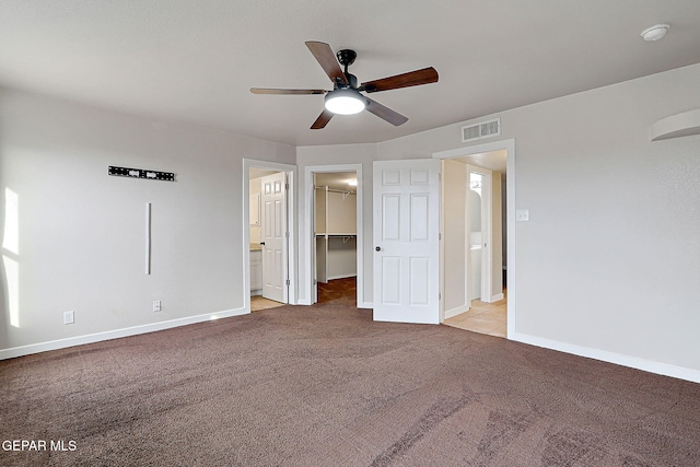 unfurnished bedroom with ceiling fan, light carpet, visible vents, baseboards, and a walk in closet