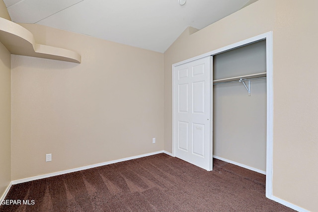 unfurnished bedroom featuring lofted ceiling, a closet, dark carpet, and baseboards