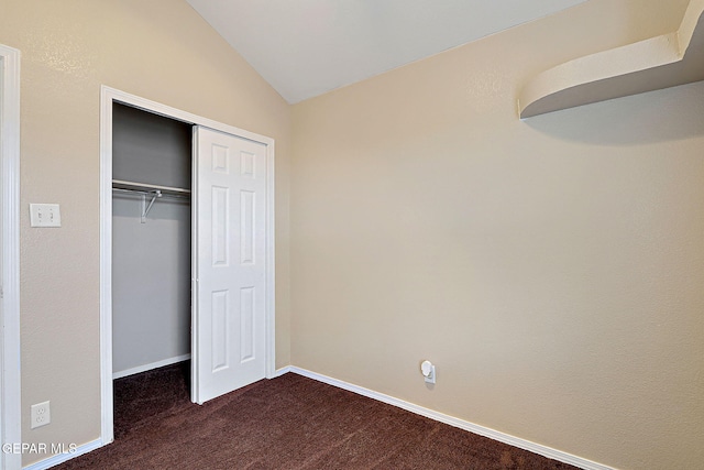 unfurnished bedroom featuring a closet, vaulted ceiling, dark carpet, and baseboards