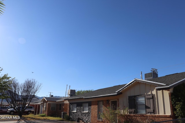 view of side of home with central AC unit, a chimney, fence, board and batten siding, and brick siding