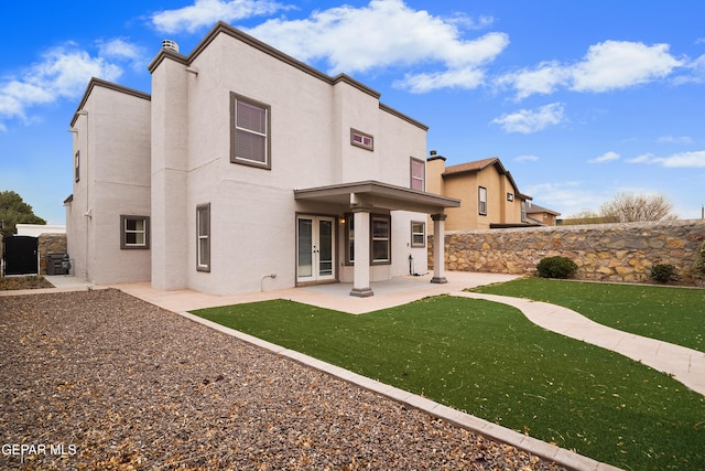 back of house featuring french doors, a chimney, stucco siding, a lawn, and a patio area