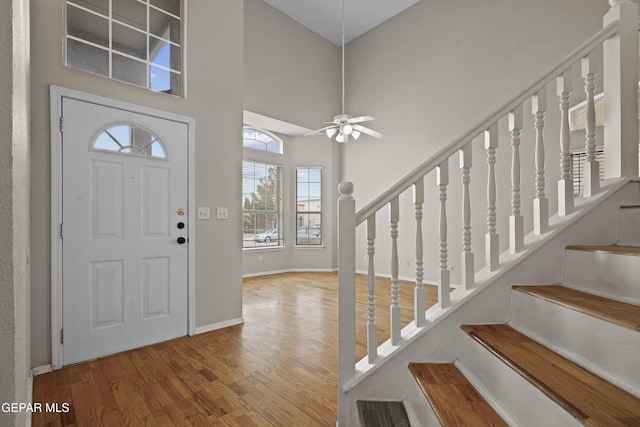 foyer entrance with wood finished floors, a towering ceiling, a ceiling fan, stairs, and baseboards