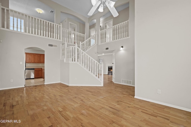 unfurnished living room featuring a lit fireplace, light wood finished floors, visible vents, and a ceiling fan